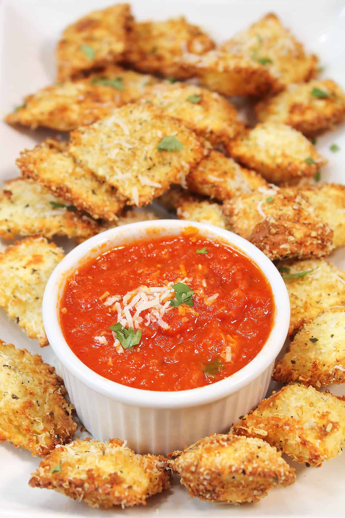 Bowl of marinara with air fryer ravioli around it.