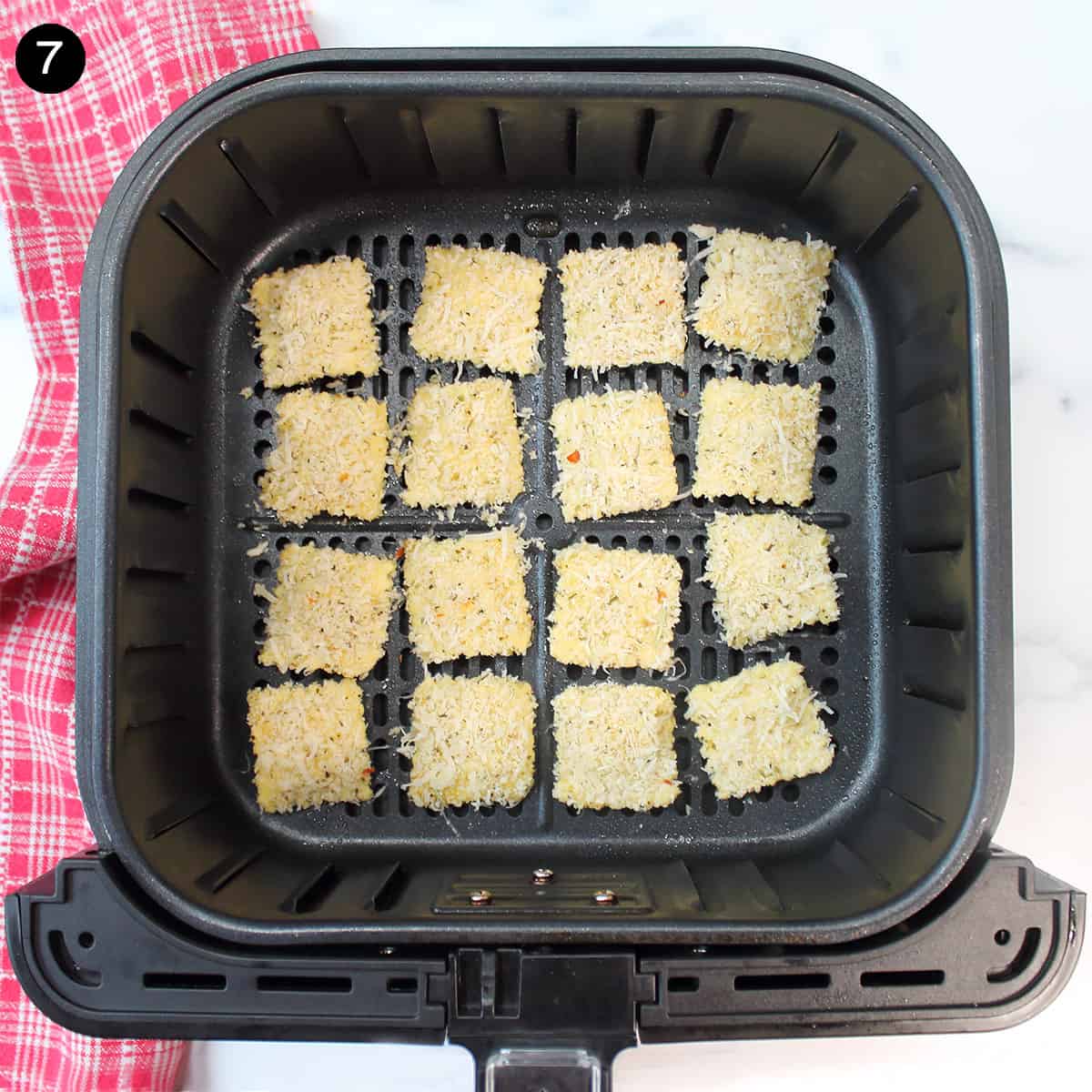 Breaded ravioli in air fryer basket.