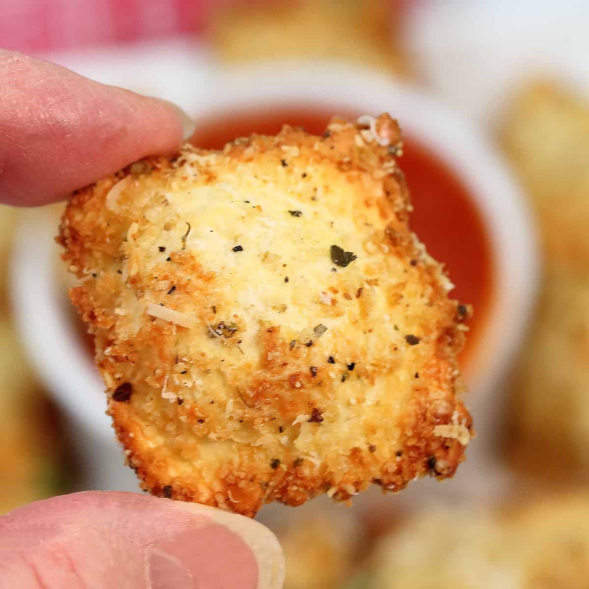 Holding air fried ravioli showing golden brown crispiness.