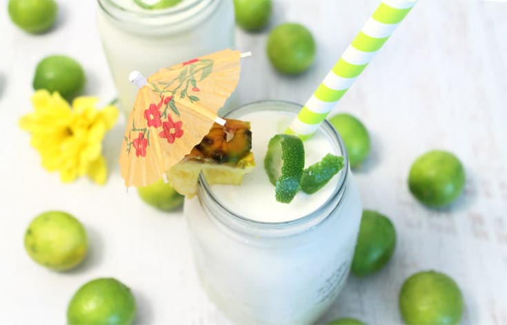 Overhead of foamy colada with cocktail umbrella and surrounded by key limes.