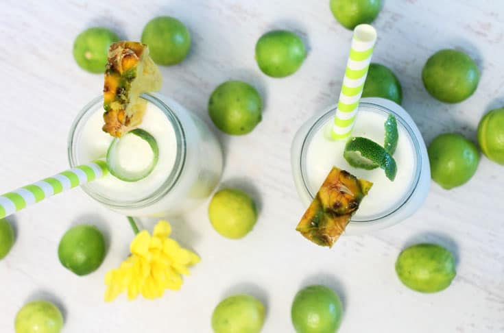 Overhead of 2 key lime coladas on white table and surrounded by key limes.