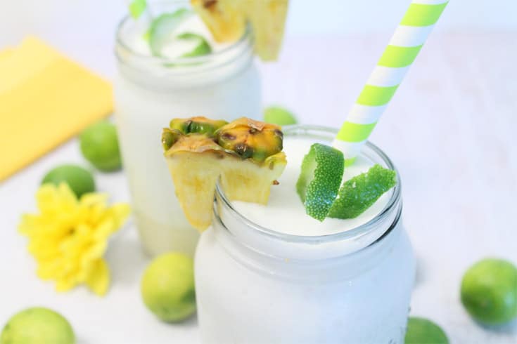 Closeup of colada showing frothy contents with lime curl and piece of pineapple as garnish.