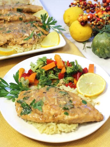 Lemon chicken on white plate with serving of vegetables.