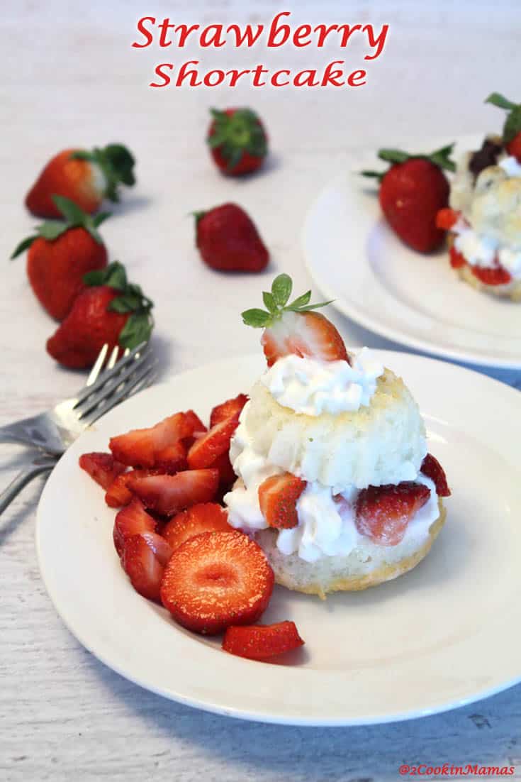 Strawberry shortcake filled with whipped cream and strawberries on a white plate with strawberries on the side.