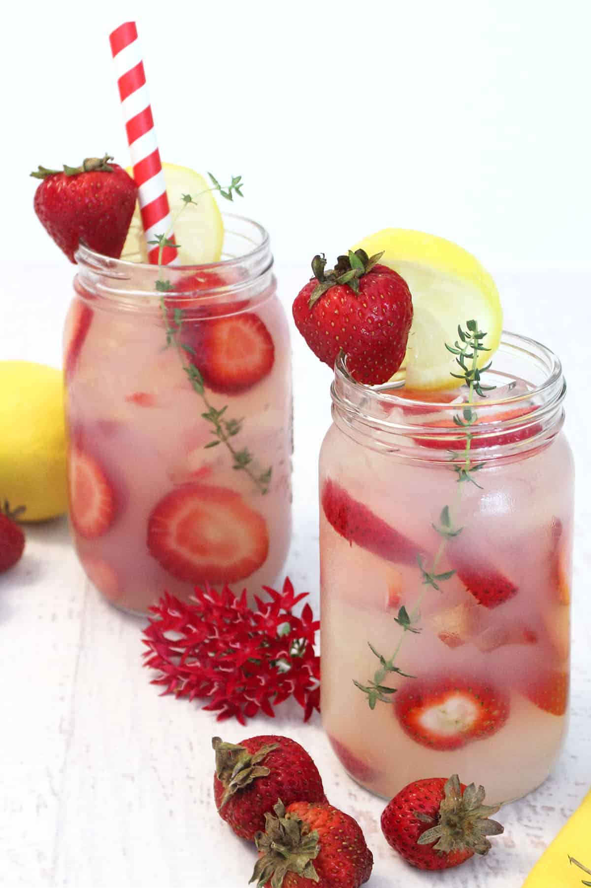 2 mason jars filled with lemonade and garnished with strawberry, lemon slice and red and white striped straw.