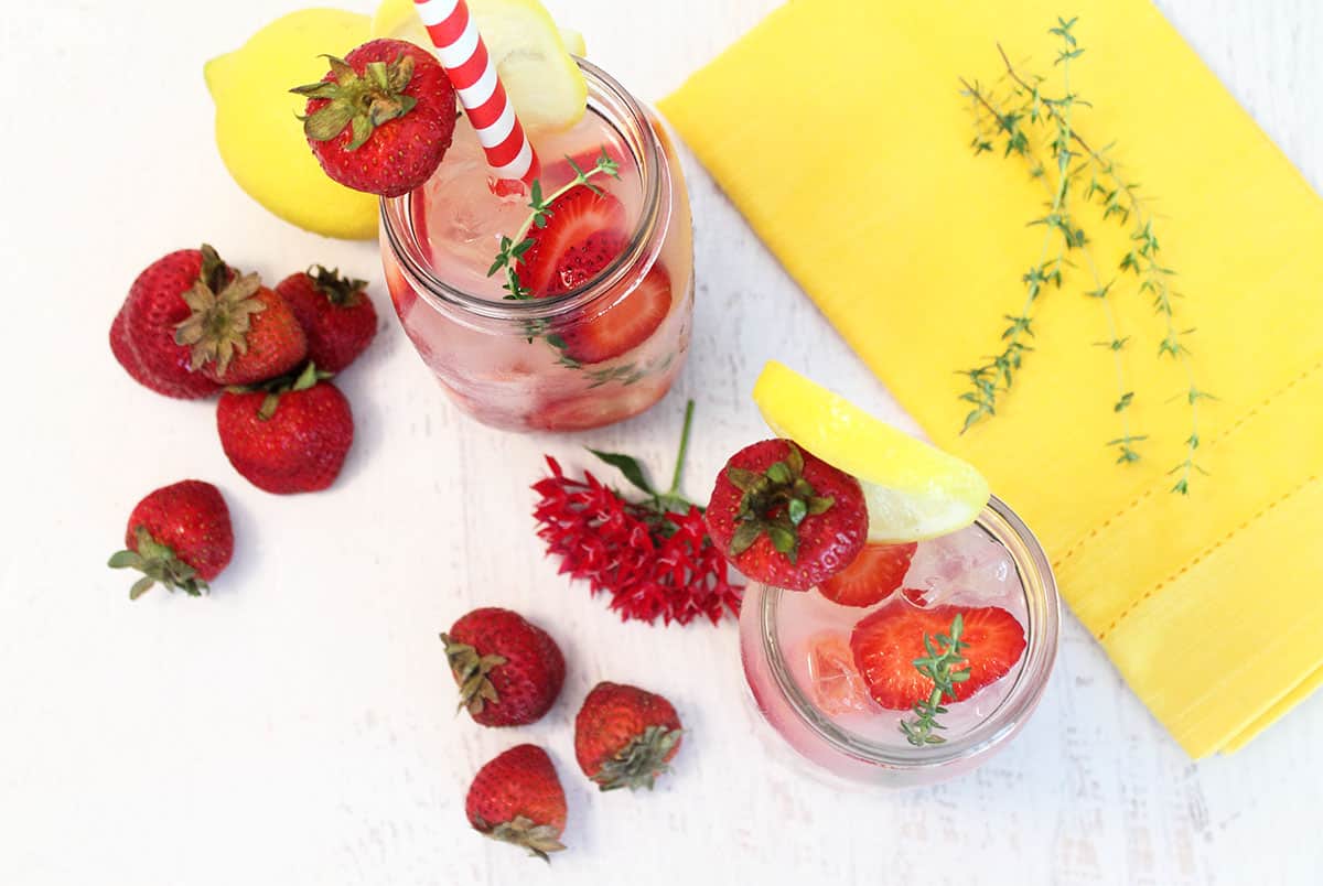 Overhead shot of filled mason jars with strawberries around it and a yello napkin with a thyme sprig on it.