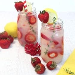 2 glasses of vodka lemonade showing sliced strawberries floating in drink with strawberries and lemon beside them.