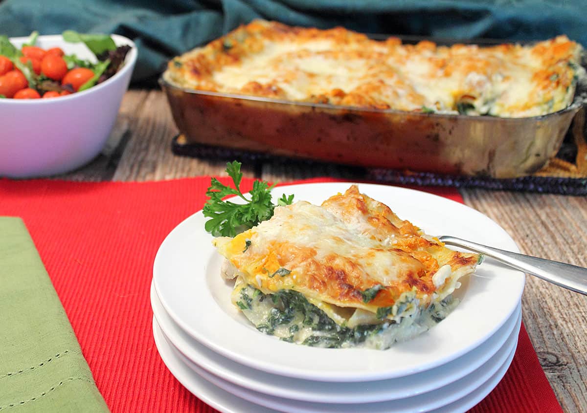 Creamy Chicken Lasagna on white plate with full casserole and salad in background.