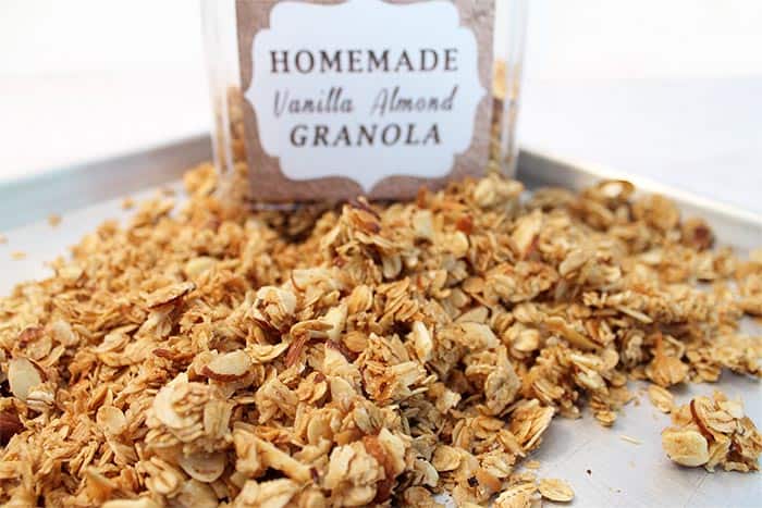 Labeled container in back of baked vanilla almond granola on cookie sheet.