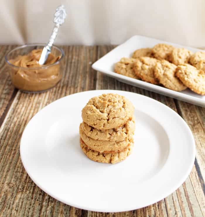 Stacked cookies on white plate with platter of cookies and bowl of peanut butter in background.