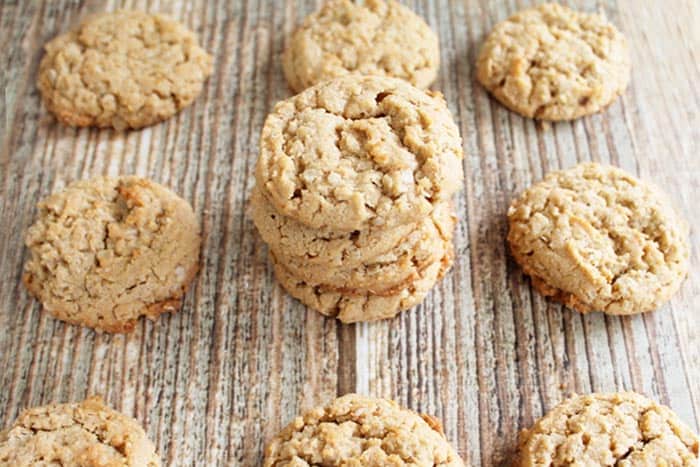 3 cookies stacked on wooden table with more cookies around them. 