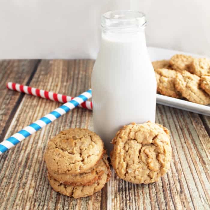 PB cookies in front of jug of milk with blue and red striped straws to side.