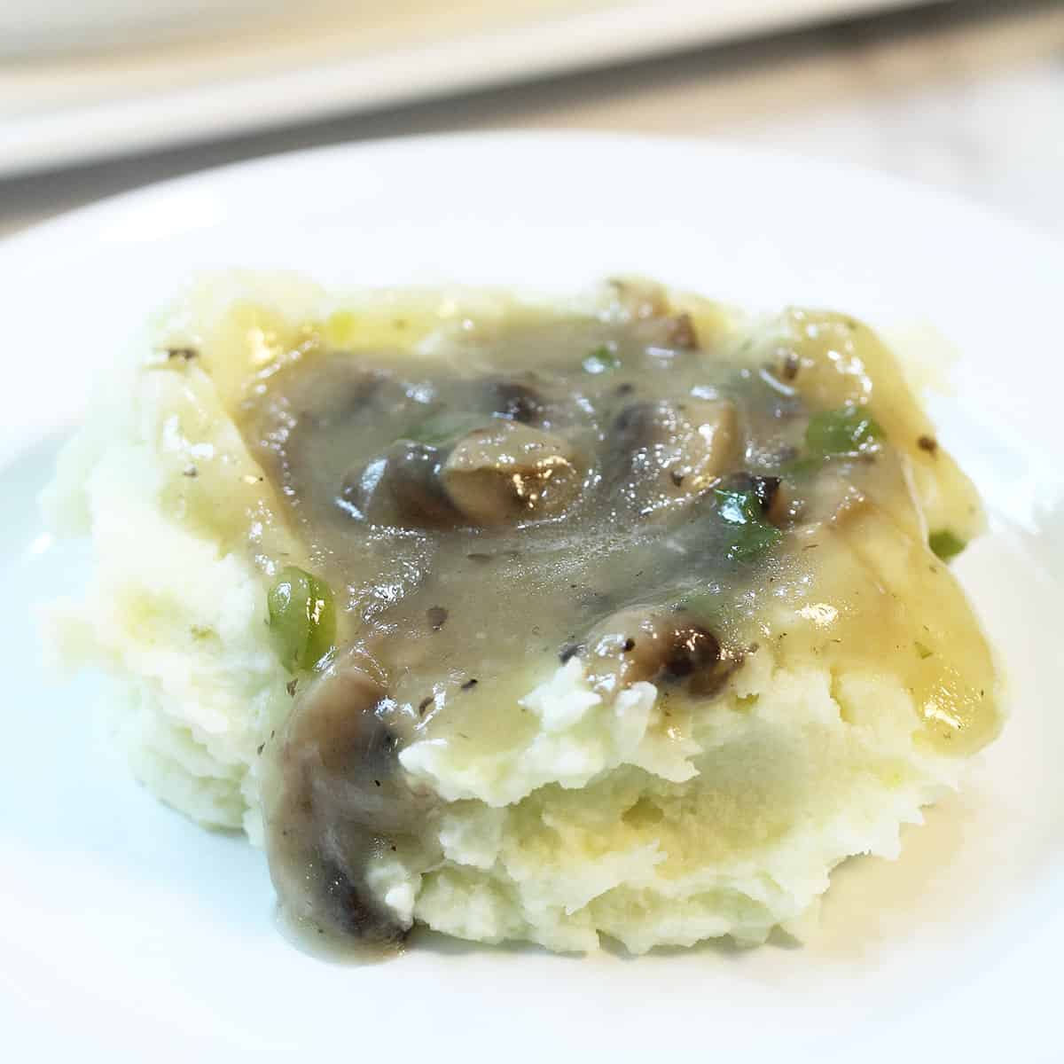 Gravy topped potatoes on white plate.