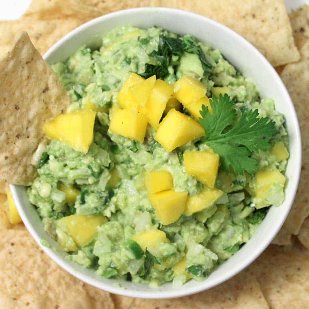 Overhead of Mango Pineapple Guacamole in white bowl with tortilla chip in dip.