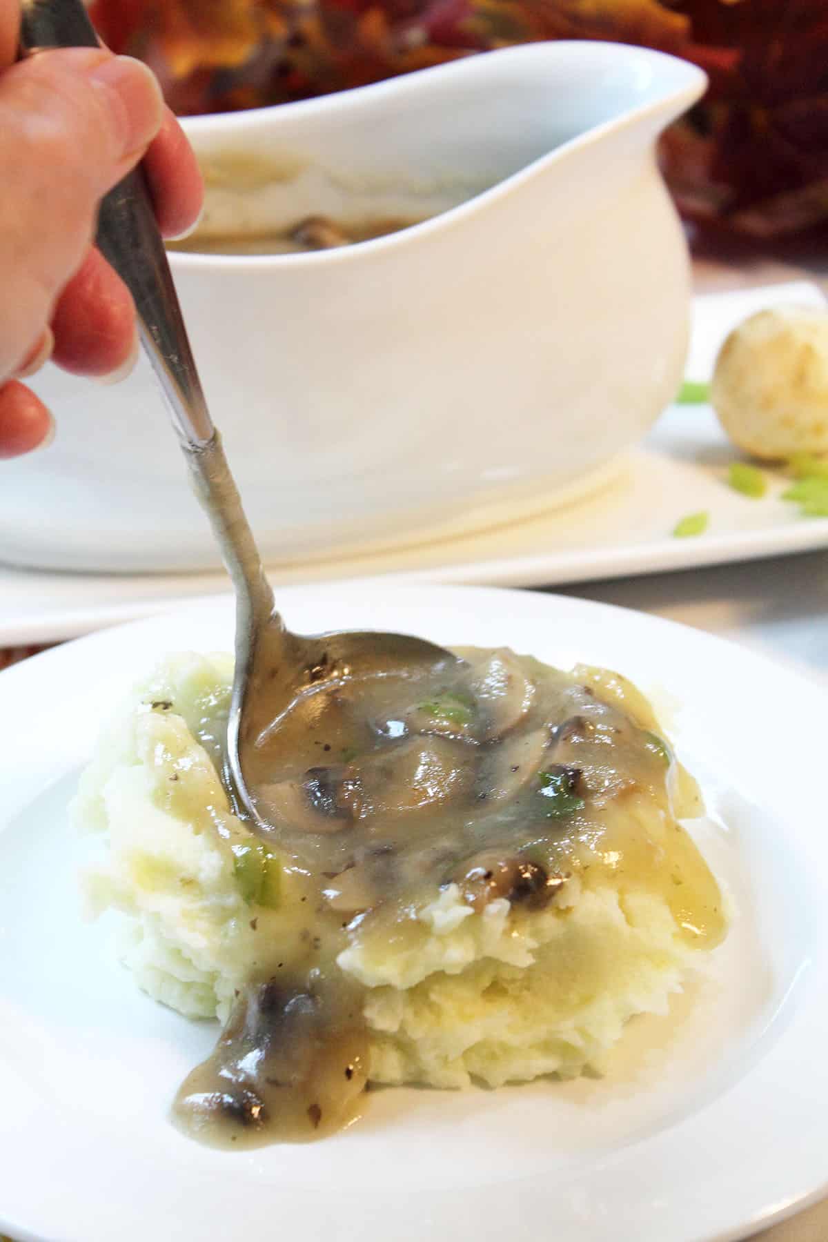 Ladling gravy into pile of mashed potatoes with gravy boat in background.