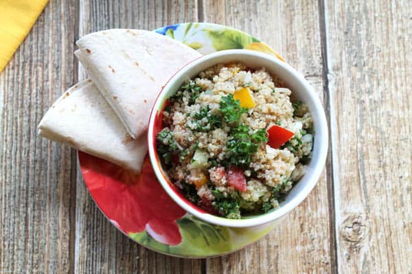 Overhead of tabouli 2 in bowl on flowery plate with folded pita on side.