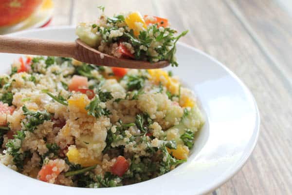 Quinoa Tabouli in wide bowl with serving on wooden spoon.