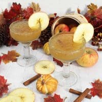 2 Apple Cider Margaritas with apple slice garnish and fall leaves behind them.