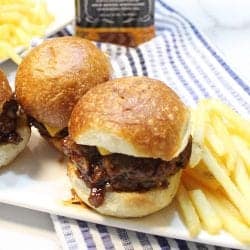 Mini burgers sliders with jack daniels bbq sauce on white plate with fries.