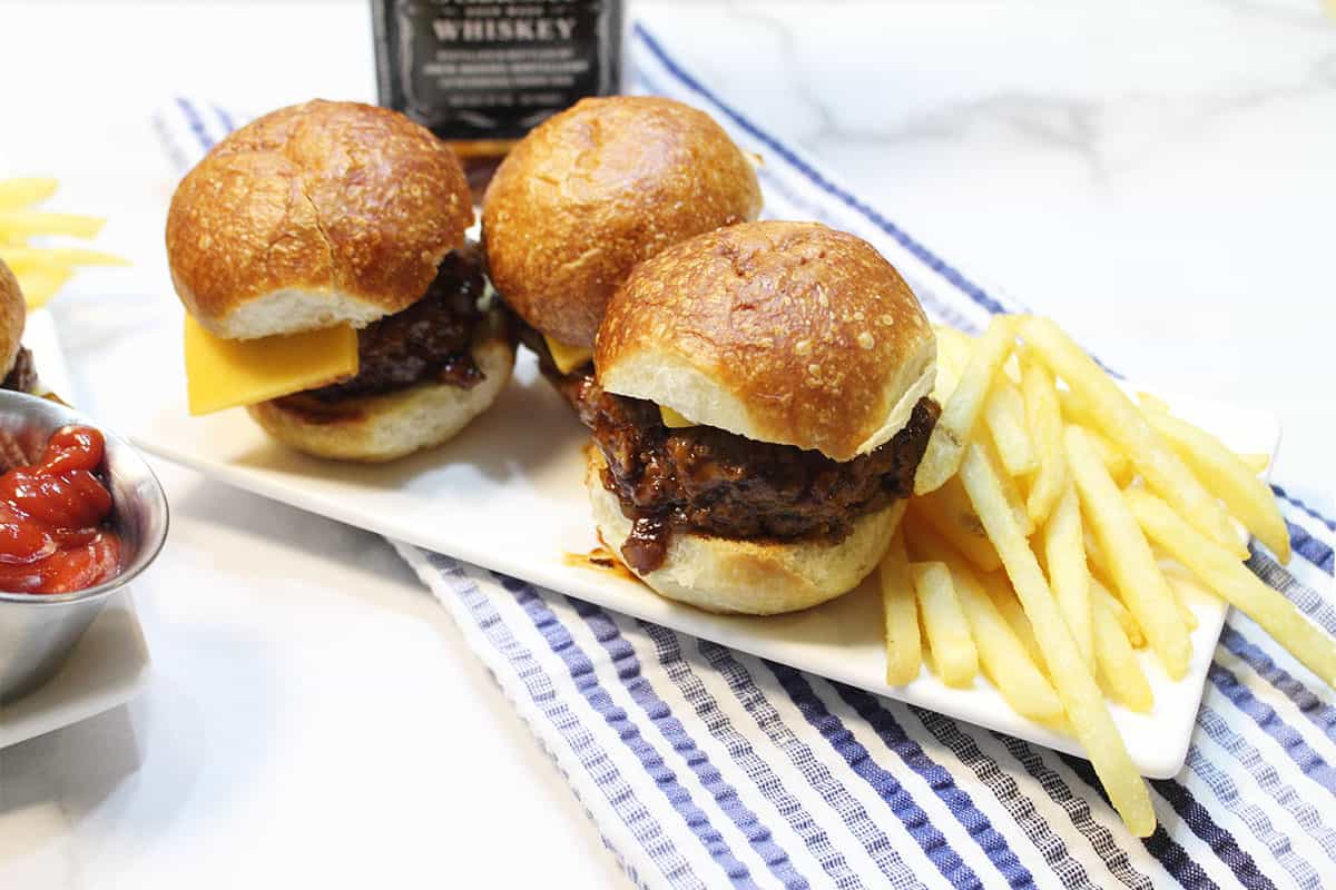 Mini Burgers Sliders on rolls on white plate with fries.
