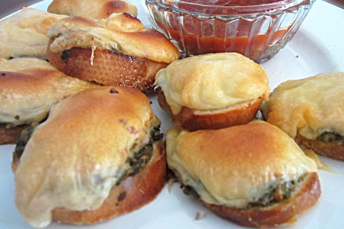 Browned cheese on top of pesto and bread on white plate with Ketchup on side.