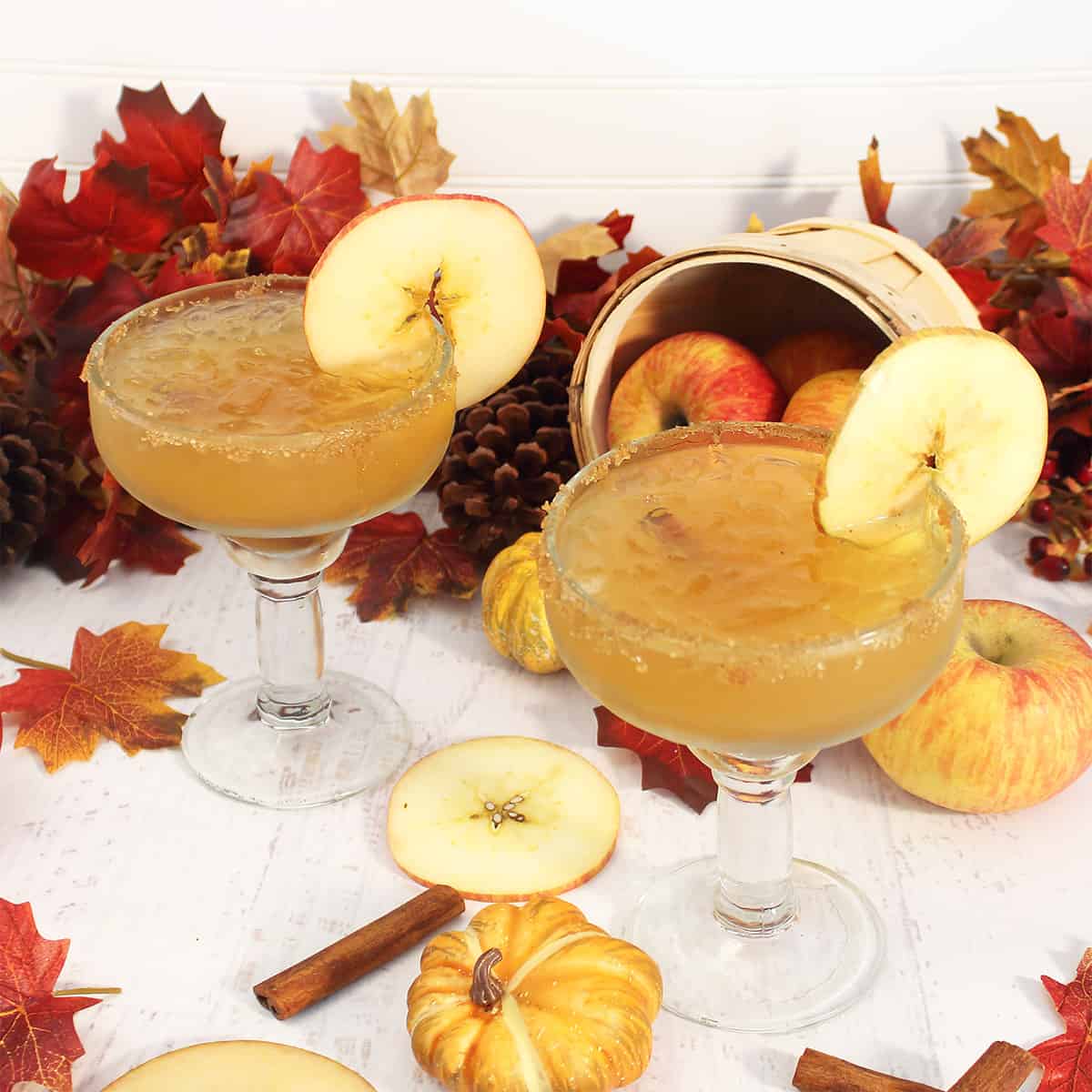 Two fall margaritas among fall leaves and basket of apples.