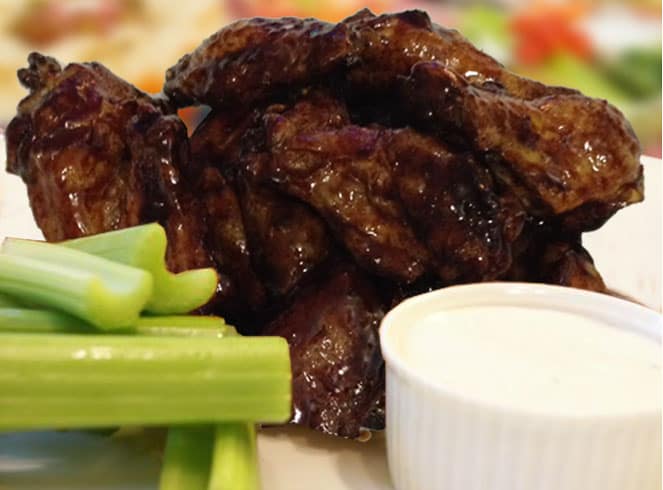 Baked chicken wings with asian sauce on white plate with celery sticks.