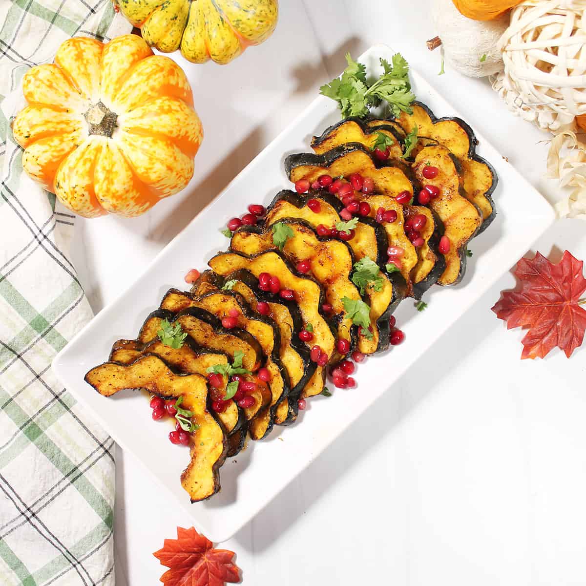 Grilled acorn squash on platter with parsley and pomegranate garnish.