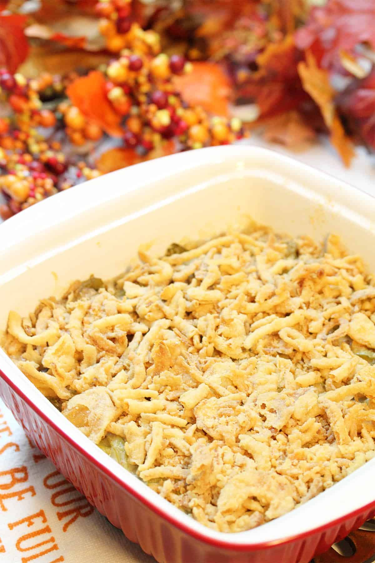 Baked creamy green bean casserole in front of fall berries and leaves.