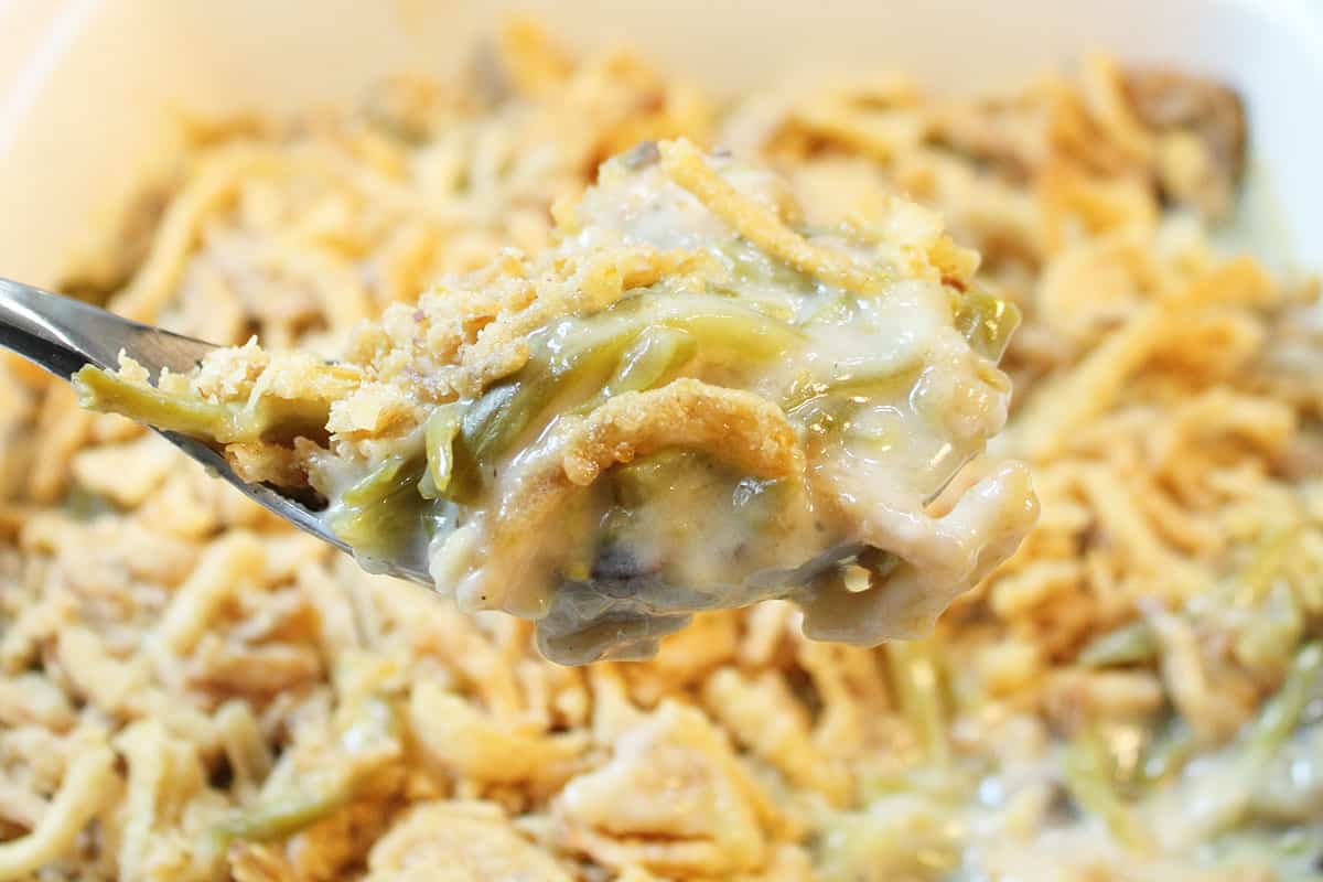 Closeup of spoonful of green beans over hot casserole.