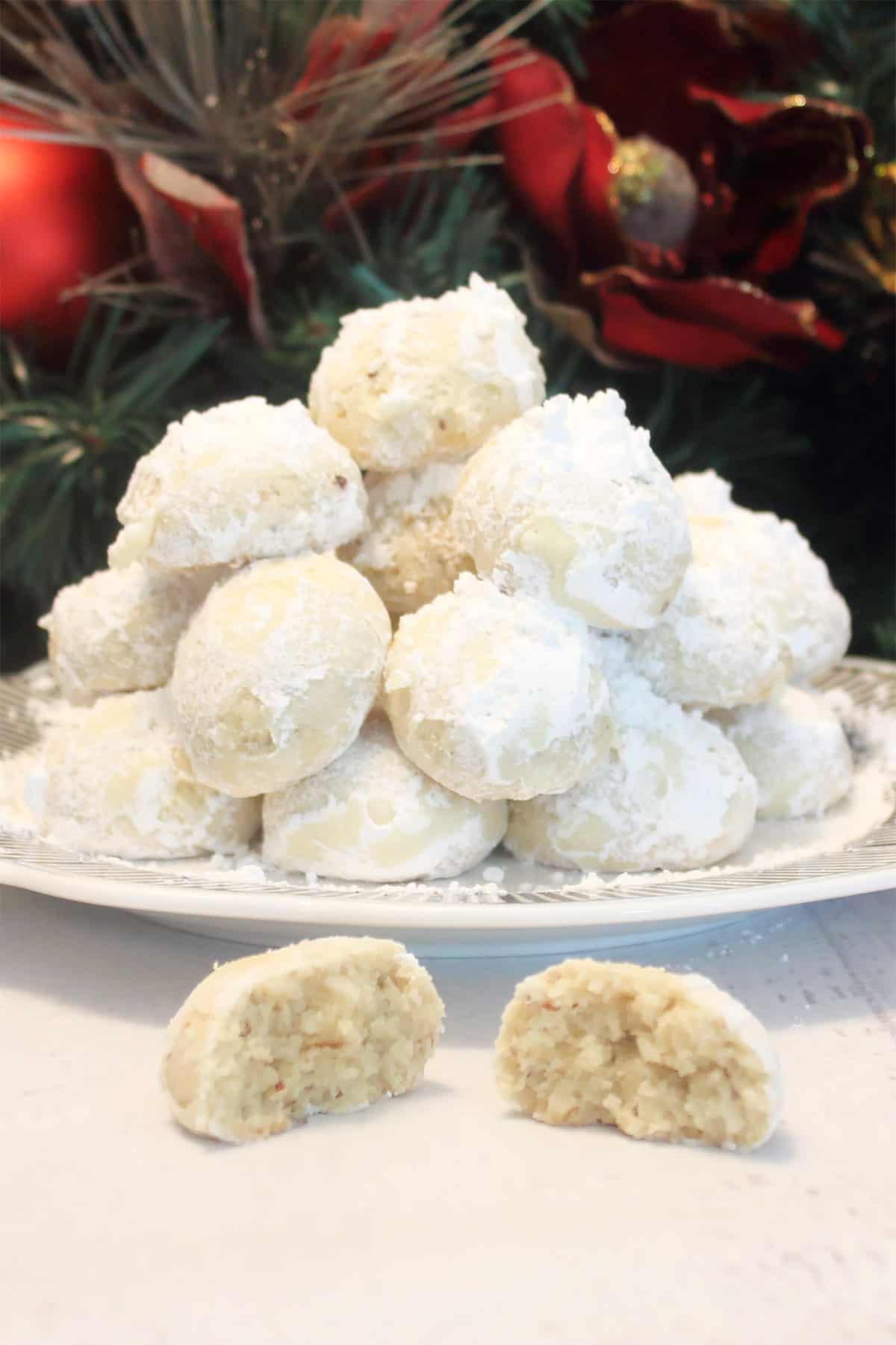Christmas Snowball Cookies piled on a cookie plate with halved cookie in front.