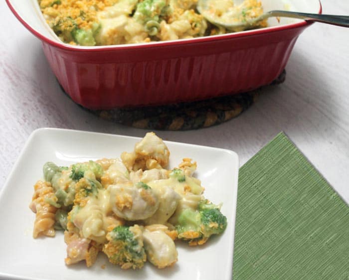 Plated Chicken Broccoli Pasta Casserole with casserole in back and green napkin beside plate.