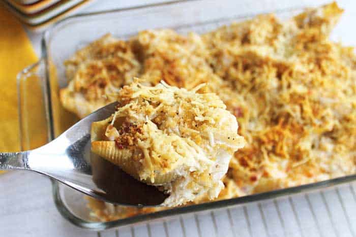 Serving up stuffed shells on large spoon above casserole.