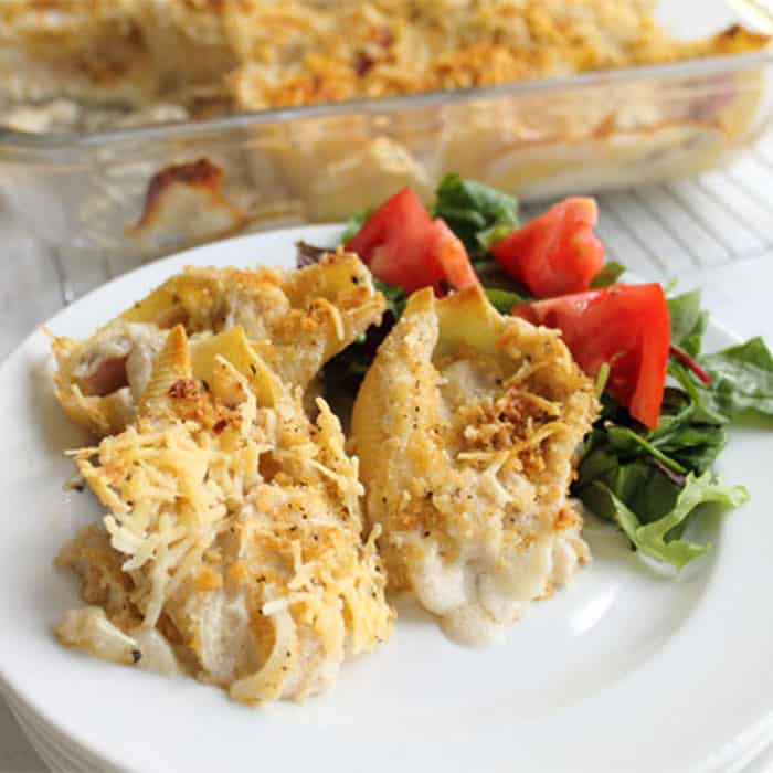 Chicken and Ham Shells plated on white plate with chopped lettuce and tomato on side.