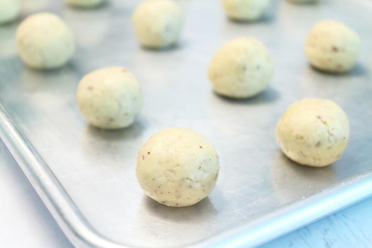 Closeup of unbaked nut ball cookies on cookie sheet. 