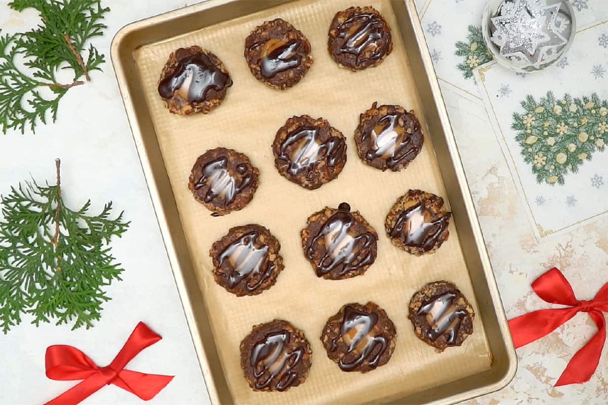 Turtle Thumbprint Cookies filled with caramel and drizzled with chocolate cookies on cookie sheet.