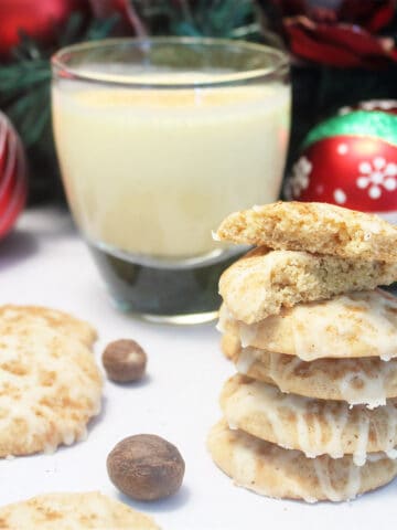 Stack of cookies next to glass of eggnog with top cookie halved.