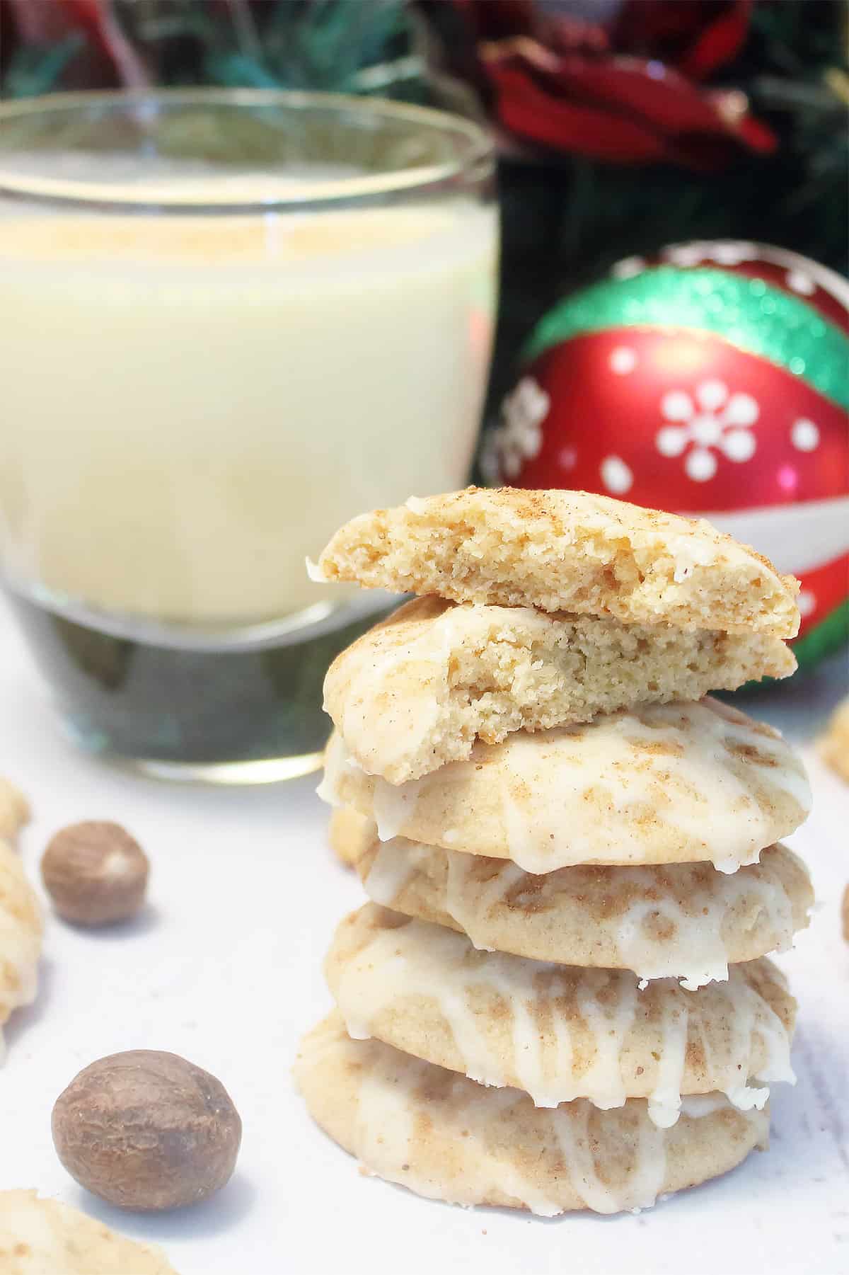 Stack of eggnog cookies with eggnog icing by glass of eggnog.