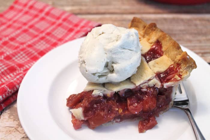 Closeup of cherry pie with ice cream on top next to red checkered towel.