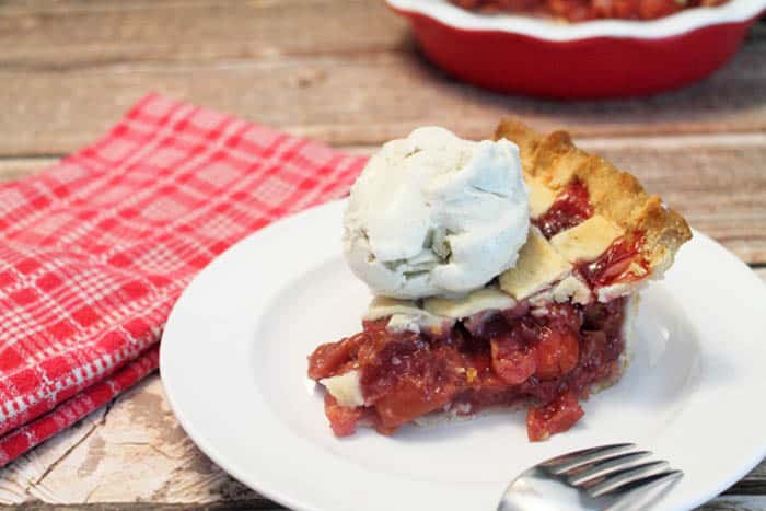 Slice of pie on white plate with ice cream on top.