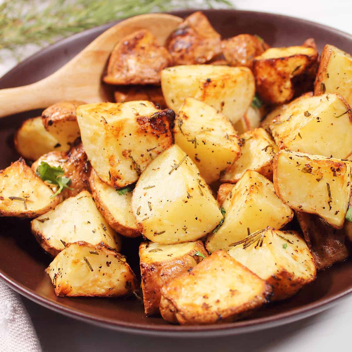 Closeup of golden potatoes in brown bowl with wooden spoon.