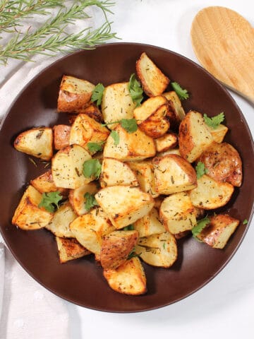 Garnished rosemary potatoes in brown bowl.