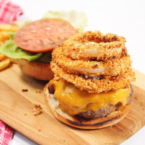 Rodeo Burger topped with onion rings on wooden board.