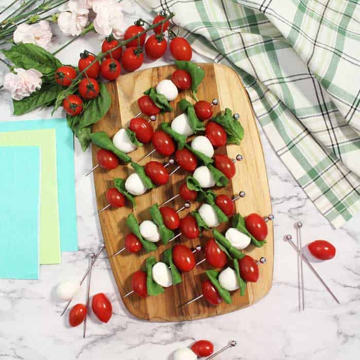 Tomato, basil and mozzarella threaded on skewers on wooden cutting board with tomatoes on vine in background