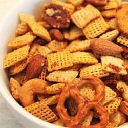 Closeup of GF Chex Mix in white bowl showing pretzels, chex square, pretzels and nuts.
