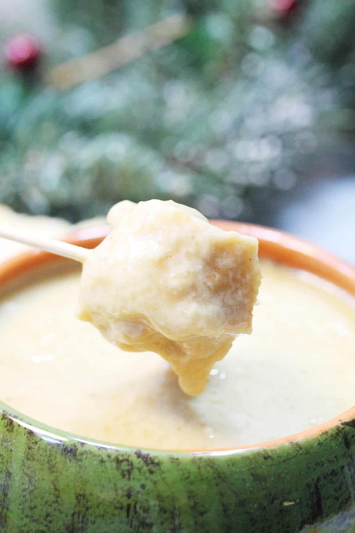 Closeup dipping bread into melting pot cheddar cheese fondue.