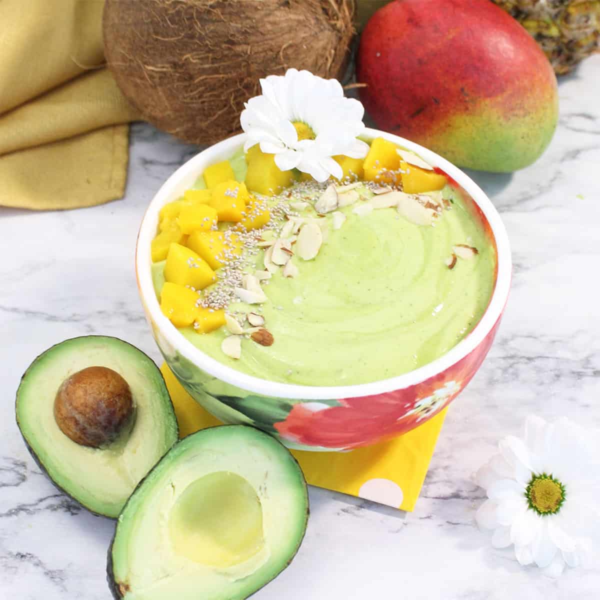 Mango green smoothie bowl with almonds mango and chia seed garnish and fruit all around.
