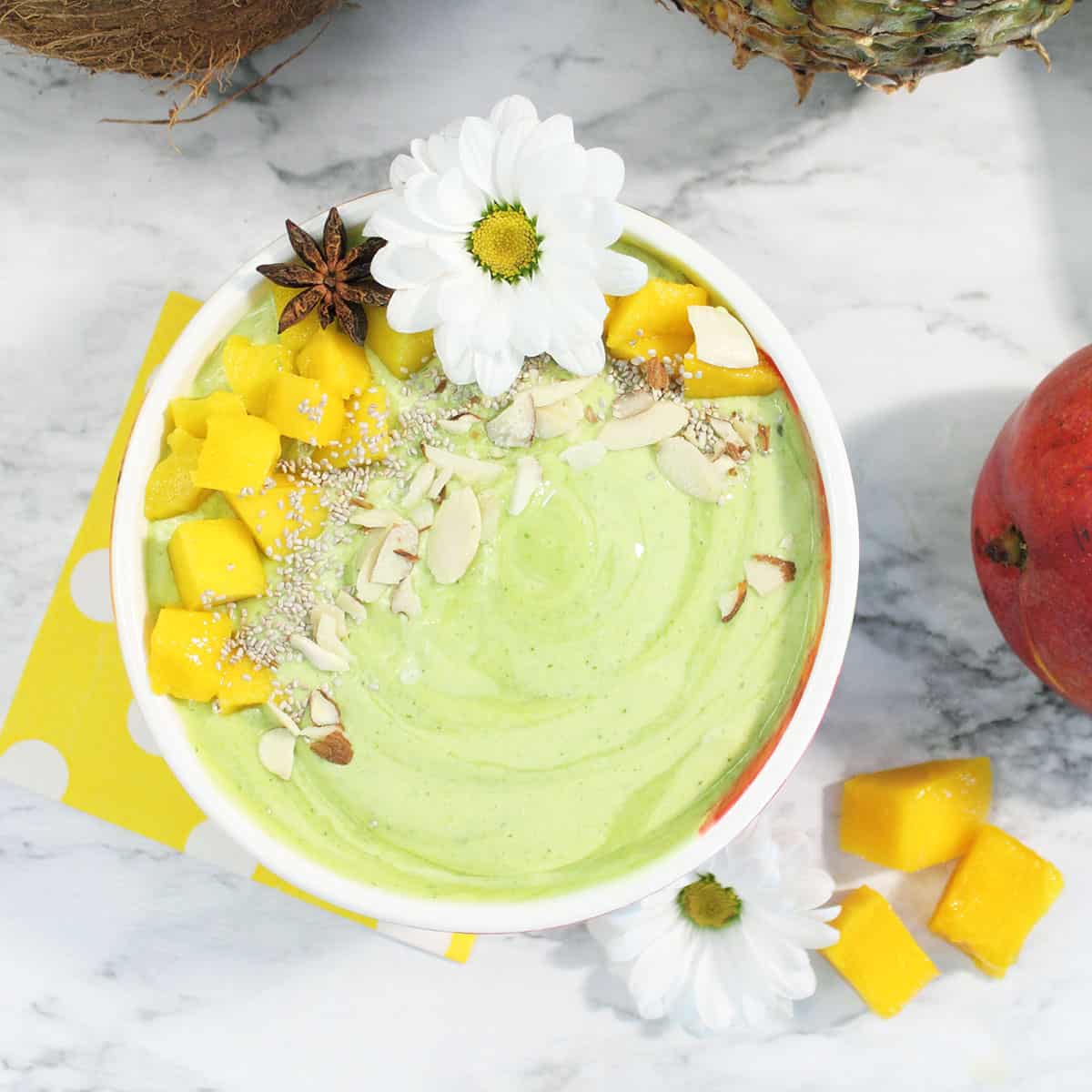 Green Pina Colada Smoothie in bowl on white table with mango pieces around bowl.