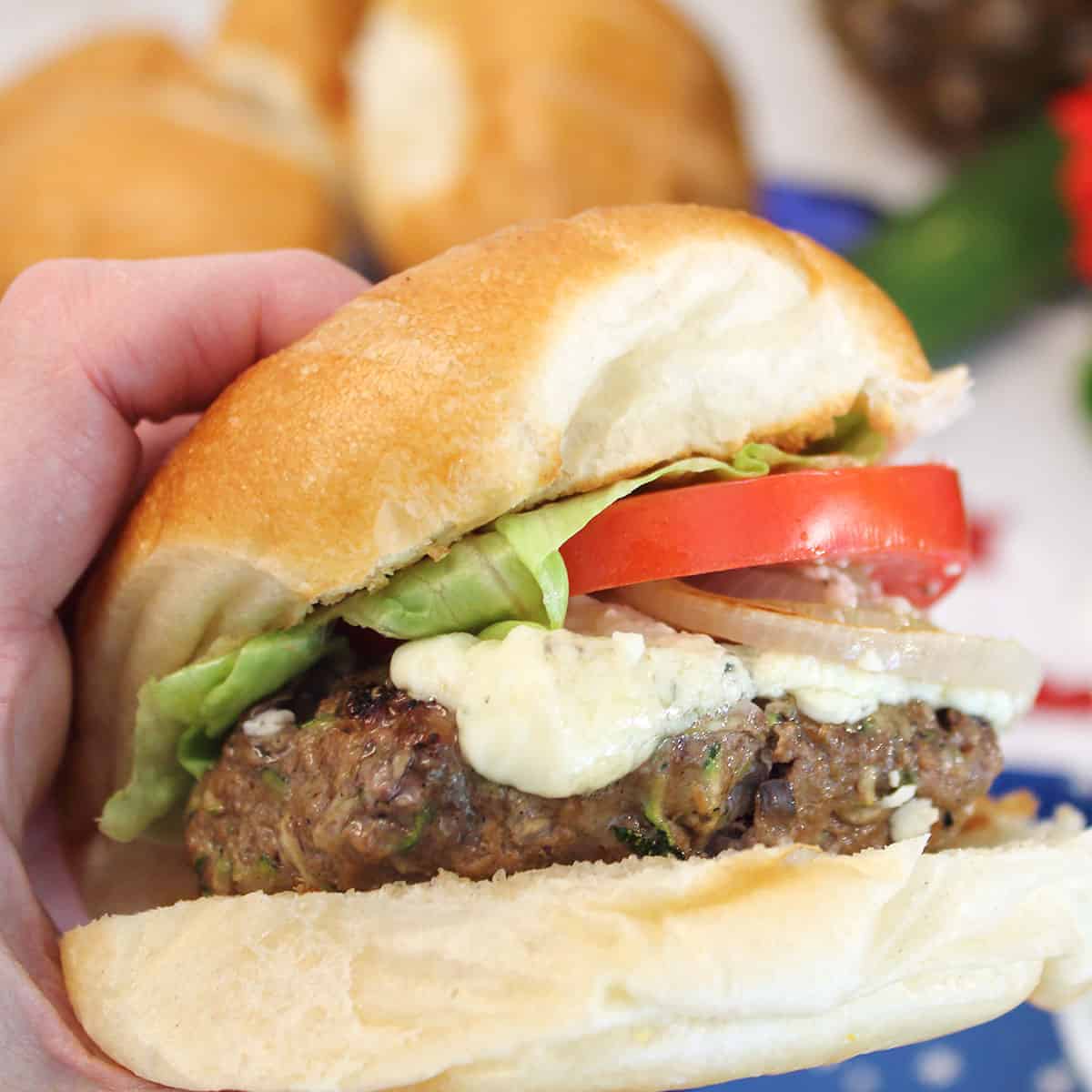 Holding a burger with melted blue cheese with both hands.
