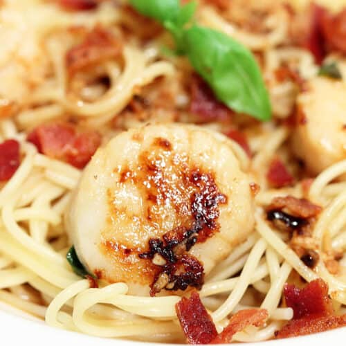 Closeup of scallop with bacon on top of pasta